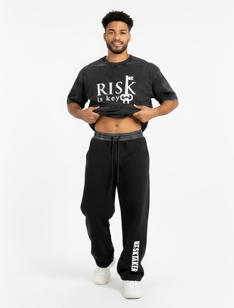 A front-facing studio shot of a model showcasing the unique silhouette of the barrel-leg sweatpants. The model is lifting both sides of their outer top or hands slightly to fully expose the wide, eye-catching black and white plaid contrast waistband. The sweatpants are styled in a loose, oversized fit, showcasing how the heavyweight fleece bows out at the thighs before tapering cleanly at the ribbed ankle cuffs. The model wears the sweatpants pulled up to a mid-rise fit, highlighting the white adjustable dr