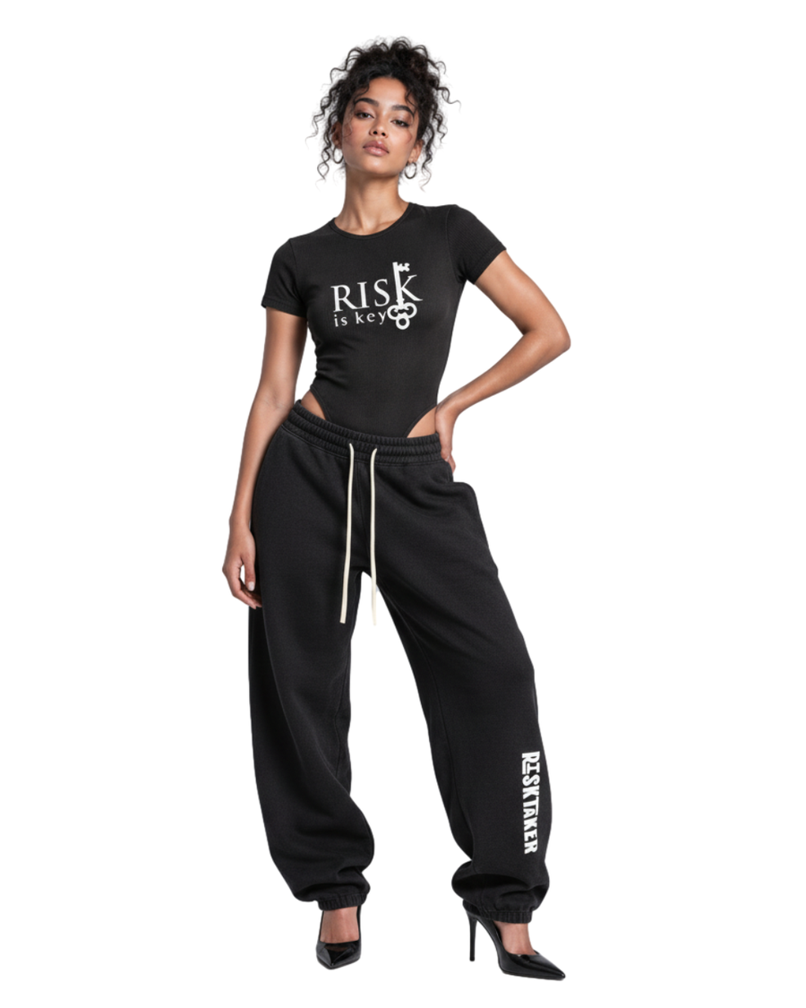 Woman wearing the black mineral wash Riskey Business short-sleeve bodysuit styled with slouchy barrel sweatpants and pointed-toe heels.