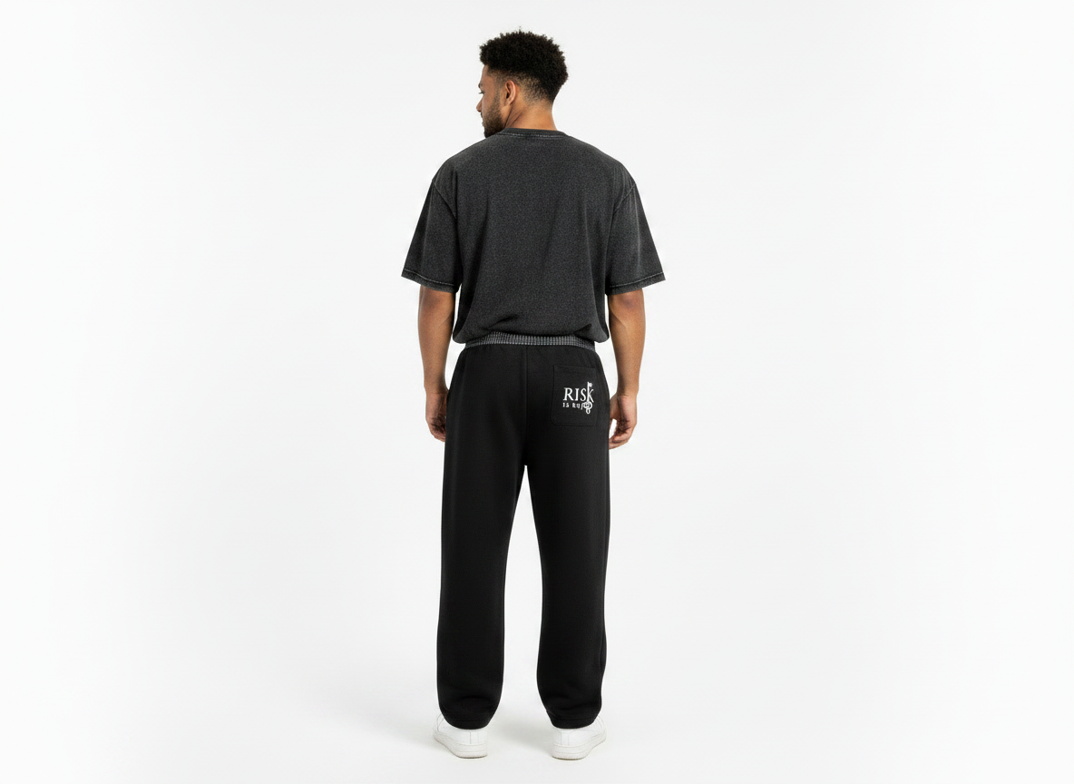 A back-view product mockup featuring a model wearing the heavyweight streetwear joggers. The image highlights the clean back construction of the pants, showing how the fabric drapes smoothly over the hips and legs without rear pockets. The black and white plaid flannel fabric continues entirely around the back of the waistband, creating a distinct, mock-layered aesthetic. The volume of the curved barrel-leg cut is visible from behind, tapering down sharply to sit neatly above the model's footwear.