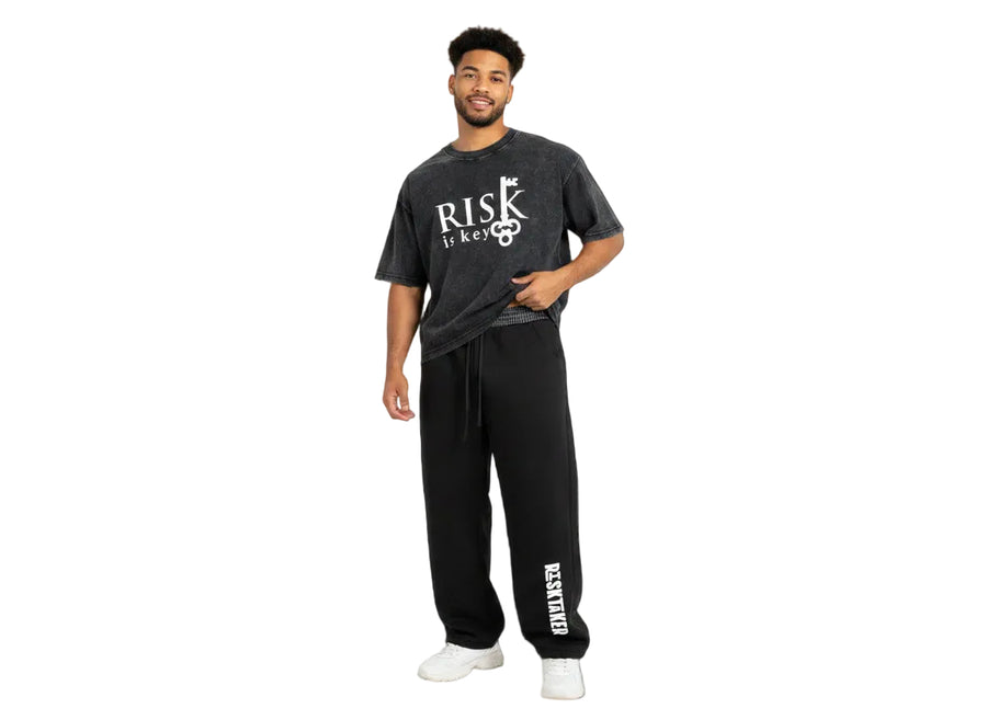 Gen z Male wearing a black black mineral wash t-shirt and pants with RISK is Key logo branding on a white background