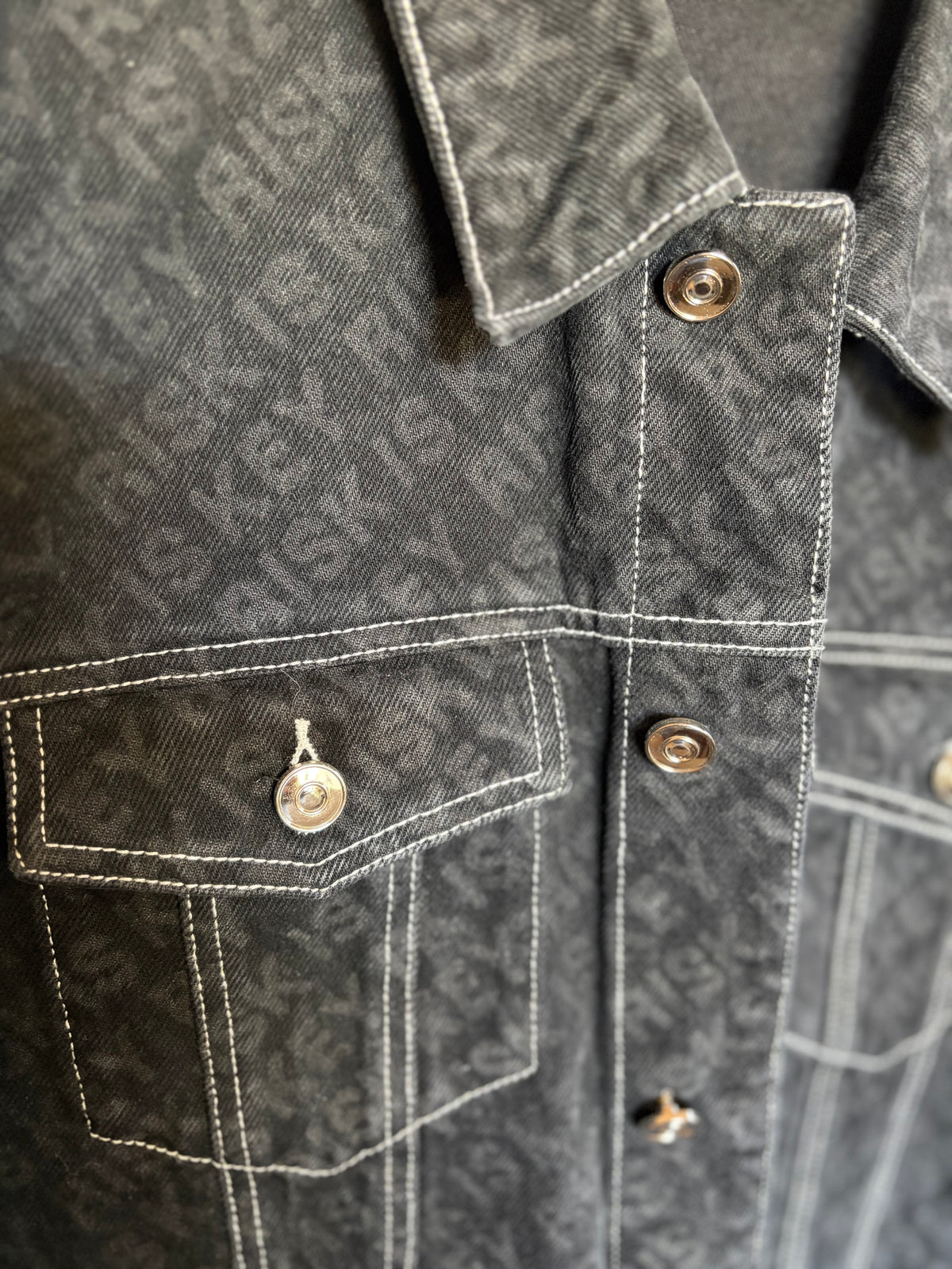 Close-up of the high-quality black denim fabric and white "Risk Is Key" repeat logo print on the Pack Leader jacket.